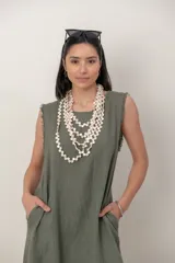 Vestido largo de lino color verde militar, sin mangas, con cuello redondo y bolsillos laterales. Presenta detalles desflecados en las sisas y en el dobladillo asimétrico.