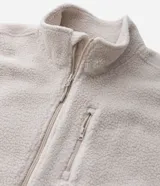 Campera deportiva de sherpa color beige, con cuello alto, cierre frontal completo y bolsillo con cierre en el pecho. Presenta un corte boxy holgado, mangas largas y acabado de textura suave.