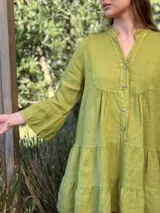 Vestido amplio de lino color verde lima, con cuello mao y abertura frontal con botones de coco. Presenta un diseño con canesú fruncido y volados en los puños de las mangas largas.