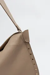 Bolso negro tipo hobo de símil cuero con textura suave y tachas metálicas en los bordes.