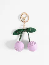 Llavero con dije de cerezas color lila, hojas verdes y herrajes dorados. Fabricado en cuero sintético.