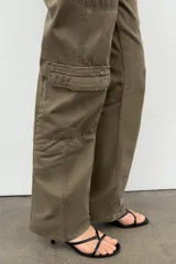 Pantalón cargo de tiro medio en color verde militar, con cierre frontal de cremallera y botones metálicos. Presenta bolsillos laterales, bolsillos de plastrón en las piernas con cierre de cremallera y trabillas en la cintura.