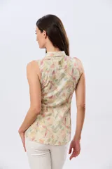 Camisa sin mangas de lino y algodón, con estampado floral en tonos violeta y verde sobre base beige, cuello camisero y cierre frontal de botones.
