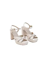 Sandalias de cuero color blanco hueso con taco forrado de 10 cm y plataforma de 2.5 cm. Presentan tiras cruzadas en la parte delantera y cierre de hebilla en el tobillo.