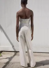 Mono largo color crudo, sin mangas, con cuello escotado, trabillas, cinturón desmontable y bolsillos laterales con cierre de cremallera.