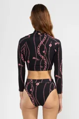 Crop top de bikini negro con estampado de cadenas rosadas, cierre frontal con tirador de flor, cuello alto y mangas largas.
