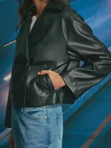 Chaqueta corta de cuero sintético en color negro, con diseño de doble botonadura, solapas amplias y corte holgado.
