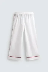 Pijama de dos piezas confeccionado en popelín de algodón blanco, con vivos de ribete en color bordó. Incluye una camisa de manga larga con cuello bowling, bolsillos de plastrón y cierre frontal de botones, y un pantalón de corte relajado con cintura elástica y bolsillos laterales.