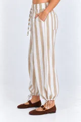 Pantalón a rayas beige y blancas con cintura elástica, bolsillos laterales y traseros, corte holgado con piernas globo y cordón de ajuste en los tobillos.