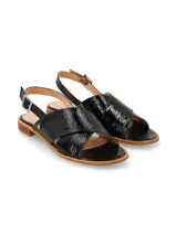 Sandalia de cuero charol negro con tiras anchas cruzadas en el empeine y tira trasera con hebilla metálica ajustable. Cuenta con suela plana y taco bajo de madera.