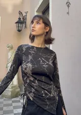Top de manga larga color negro, confeccionado en jersey elástico. Presenta un diseño asimétrico con jaretas laterales regulables que permiten ajustar el largo y el volumen, y aberturas para los pulgares en los puños.
