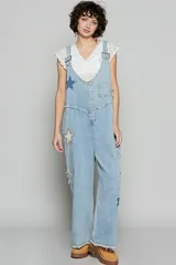 Mono denim celeste con tirantes amplios y escote en V, apliques de estrellas en varias partes, botones en el frente y un bolsillo en la parte superior sobre el pecho y dos en la parte posterior.