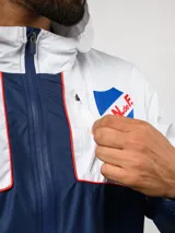 Campera de lluvia Umbro del Club Nacional de Football, con diseño de bloques de color en rojo y azul marino. Presenta capucha, cierre frontal, puños elásticos y detalles de piping blanco. Incluye logo de Umbro y escudo del club en el pecho.