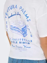 Remera blanca de manga corta con cuello redondo y estampado azul en la espalda con la leyenda "Ventura Palms Sandwich Shop" y el dibujo de un sándwich.