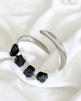 Brazalete rígido plateado con incrustaciones de piedra turmalina negra.