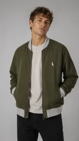 Campera bomber color verde militar con cierre frontal, puños, cuello y dobladillo en tejido elástico gris. Presenta bolsillos laterales ribeteados y un pequeño logo bordado en el pecho.