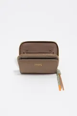 Billetera compacta de nylon color beige, con cierre de cremallera perimetral y tirador decorativo con cordón. Presenta el logo metálico de la marca en el frente.