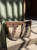 Charm decorativo para bolso compuesto por un mosquetón verde oliva, una pieza circular marrón con diseño, una etiqueta rectangular celeste con la palabra 'Uruguay' y un cordón negro con detalles en blanco y celeste.