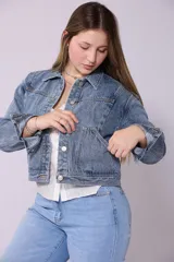 Campera de jean de mujer, color azul claro lavado, con corte cropped y estilo clásico. Presenta cuello camisero, botones metálicos frontales y bolsillos de parche en el pecho.