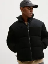 Campera puffer con cuello alto y cierre frontal, confeccionada en tejido teddy negro con paneles superiores lisos. Cuenta con bolsillos laterales y relleno de poliéster.