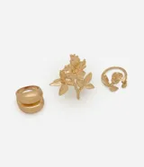 Kit de tres anillos de metal color dorado. Incluye dos anillos con diseño de flores y hojas con texturas orgánicas, y un anillo de diseño minimalista con volumen marcado.