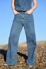 Pantalón de jean tiro alto con corte recto y holgado, confeccionado en denim azul con estampado de motivos naturales en tono azul oscuro.