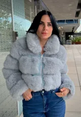Campera corta de piel sintética en color gris, con cuello alto y cierre frontal metálico. Diseño de paneles horizontales de pelo sintético con base de tela al tono.
