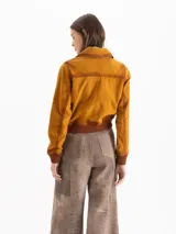 Campera bomber confeccionada en gamuza color tostado, con cierre frontal, bolsillos aplicados con solapa en el pecho y puños y cintura tejidos en marrón oscuro.