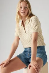 Remera color crema de tejido de punto calado, con cuello polo y mangas cortas.