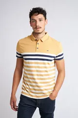 Remera tipo polo de manga corta con diseño de bloques, presentando la parte superior en color mostaza liso y la parte inferior con rayas horizontales en tonos mostaza, blanco y azul marino. Cuenta con cuello clásico, cierre frontal de tres botones y logo pequeño estampado en el pecho.