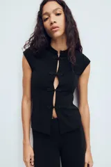 Top de tejido elástico color negro, con cuello mao, manga muy corta y cierre frontal con alamares decorativos.