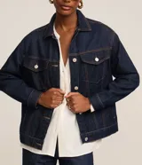 Campera trucker de jeans azul oscuro, corte amplio, con cuello clásico, cierre frontal con botones blancos, mangas largas y bolsillos delanteros con solapa.