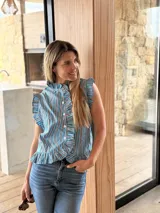 Camisa sin mangas de corte recto, con diseño a rayas verticales en tonos fucsia, azul y blanco. Presenta cuello alto, cierre frontal con botones y volados fruncidos a lo largo de la botonera y en las sisas.