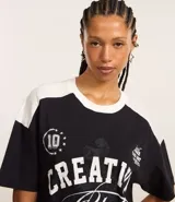 Remera oversized negra con mangas y cuello blanco, con estampado frontal que incluye la frase "Creative Club" en blanco, estrellas y otros gráficos en estilo vintage.