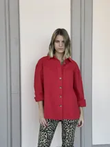 Camisa roja de corte holgado, con cuello clásico, cierre frontal con botones, mangas largas con puños abotonados, dos bolsillos con solapa en el pecho y ruedo recto.