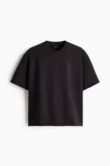 Remera boxy de algodón en punto liviano, de color negro, con hombros caídos, cuello redondo acanalado y corte oversized.