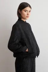 Chaqueta bomber de corte recto en tejido jacquard con estampado floral en tono sobre tono negro, cuello mao y cierre frontal de broches a presión.
