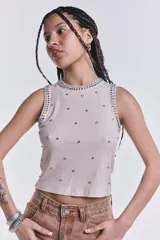 Musculosa beige de punto canalé con cuello redondo y sisa americana. Decorada con tachas y strass plateados.