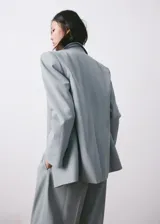 Blazer de corte sastrero en color gris azulado, con cierre frontal de un botón, solapas clásicas y bolsillos laterales con solapa.