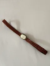 Cinto trenzado de cuero color marrón con hebilla central rectangular decorada con una piedra natural en tono claro.