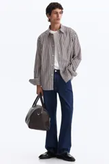 Camisa de algodón suave con cuello inglés, tapeta clásica y canesú en la espalda. Modelo de manga larga con puños abotonados y bajo levemente redondeado. Presenta diseño a rayas en tonos marrón y blanco.