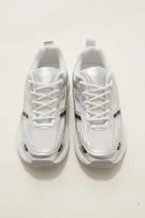 Zapatilla deportiva de estilo urbano en color blanco con detalles metalizados plateados y acentos en negro. Presenta una combinación de malla transpirable y paneles sintéticos, con suela robusta y cordones al tono.