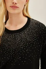 Sweater negro de manga larga con cuello redondo, decorado con apliques brillantes que simulan un degradé o salpicado en la parte superior del pecho y hombros.