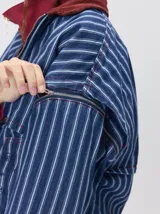 Campera de denim a rayas verticales con cuello de pana en color bordó. Presenta cierre frontal, mangas desmontables con cierre en los hombros, canesú en el pecho y bolsillos de parche cuadrados.