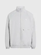 Campera deportiva Calvin Klein color gris claro, de sarga de satén brillante, con cuello alto, mangas raglán, puños y bajo elásticos, cierre de cremallera, bolsillo con cremallera en el pecho, bolsillos con botón de presión en la cintura, forro de malla transpirable y logo monograma estampado en el pecho.