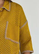 Chaqueta amarilla de tejido calado con cuello camisero, cierre con botones y bolsillo de parche en el pecho.