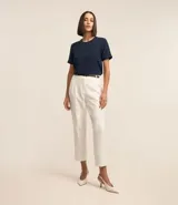 Blusa blanca de poliéster con cuello redondo, mangas cortas, cierre trasero en forma de gota, pequeñas aberturas laterales y acabados en pespuntes en las mangas y el cuello.