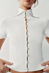 Top de punto rib color blanco, con cuello solapa, manga corta y cierre frontal con botones dorados.