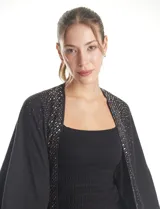 Ruana de tejido soft color negro, con detalles de brillos y tachas en los bordes frontales. Presenta una caída fluida y terminación con flecos.
