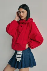 Campera parka roja estilo blouson con capucha ajustable, cierre frontal de botones a presión, bolsillos frontales con solapa y diseño holgado.